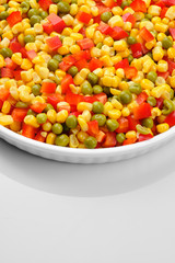 a mixture of chopped vegetables paprika, corn, peas in white plate top view	