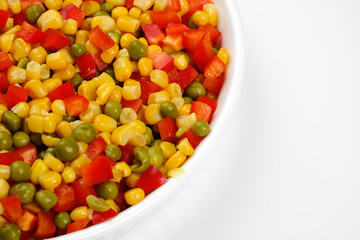a mixture of chopped vegetables paprika, corn, peas in white plate top view	