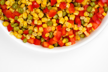 a mix of chopped vegetables paprika, corn, peas in white plate top view	