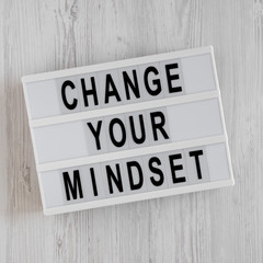 'Change your mindset' words on a lightbox on a white wooden background. Top view, from above, flat lay.
