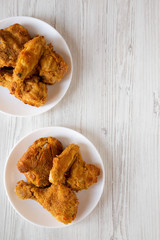 Tasty homemade oven baked fried chicken on a white plate on a white wooden background, top view. Overhead, from above, flat lay. Copy space.
