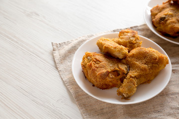 Tasty homemade oven baked fried chicken on a white plate over white wooden background, low angle view. Space for text.
