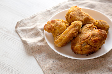 Delicious homemade oven baked fried chicken on a white plate over white wooden surface, low angle view. Copy space.