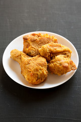 Delicious homemade oven baked fried chicken on a white plate over black surface, low angle view.