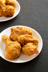 Delicious homemade oven baked fried chicken on a white plate over black background, low angle view. Copy space.
