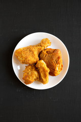 Delicious homemade oven baked fried chicken on a white plate over black background, top view. Flat lay, overhead, from above. Close-up.