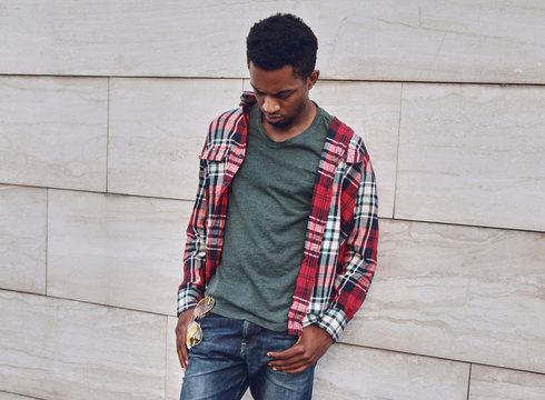 Young african man wearing casuals, red plaid shirt on city street over gray brick wall background