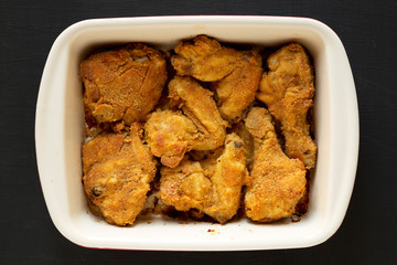 Tasty homemade oven baked fried chicken in a dish over black background, top view. Flat lay, overhead, from above.