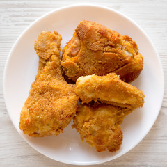 Delicious homemade oven baked fried chicken on a white plate on a white wooden background, top view. Overhead, from above, flat lay. Closeup.