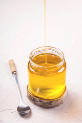 Ghee or clarified butter in a glass jar on a neutral textured background next to a spoon.