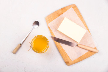 Ghee or clarified butter in a glass jar on a neutral textured background next to a spoon.