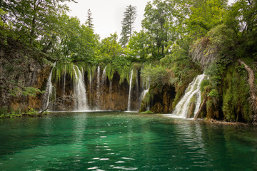 Fototapeta na wymiar Landscape view on the waterfalls and lake in Plitvice Lakes National Park on a cloudy summer day. Waterscape, nature background. Croatia.