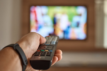 Man watching TV in the room and switches channels using the remote control in his hand