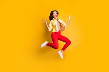Fototapeta na wymiar Full length body size turned photo of cheerful shouting woman showing horned fingers rock sign in red pants wearing white shoes isolated vivid color background