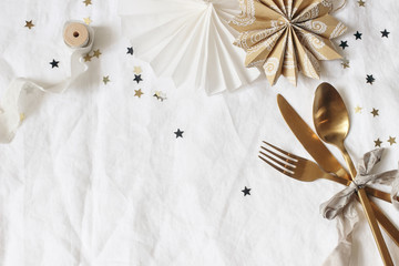 Christmas, New Year composition. Decorative table setting. Paper stars, golden cutlery and confetti stars on white linen background. Celebration, birthday party concept. Flat lay, top view, copy space