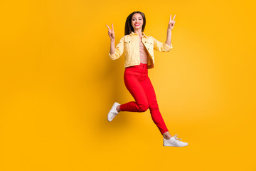 Fototapeta na wymiar Turned full length body size photo of cheerful stylish trendy white woman showing double v-sign in red pants smile toothy jumping isolated vivid color background