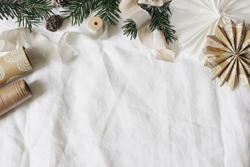Christmas frame, web banner. Fir tree branches, gift wrapping paper, silk ribbons and decorative paper stars on white linen tablecloth background. Winter festive composition. Flat lay, top view.