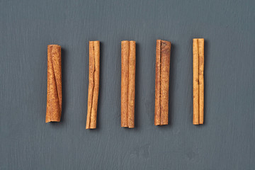 Row of five flavour cinnamon sticks lies on dark scratched desk on kitchen. Top view. Close-up