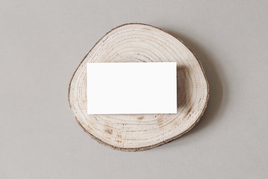 Blank white business card mockup on wooden plate, chop board. Grey table backgound. Modern minimalist template. Branding identity. Natural winter design. Flat lay, top view.