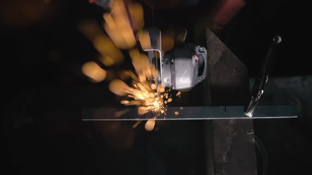 Forge workshop. Smithy manual production. Sparks fly straight in the camera against a black background. Close up details of sparks, industrial worker using angle grinder and cutting steel.