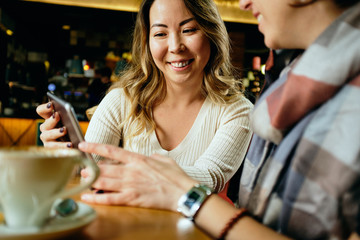 Two female friends in a cafe having coffee, smiling and chatting