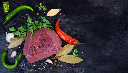 Background of piece uncooked beef among spices on black surface