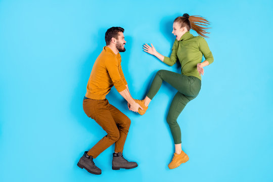 Side profile top above high angle view photo full length body size photo of crazy excited playful spouses with man taking foot and throwing his girl while lying isolated pastel blue color background