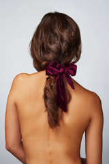 Close-up back shot of a brunette lady with a burgundy velure hair scarf fixed on the scrunchie. The...