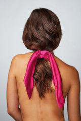 Close-up back shot of a brunette lady with a fuschia silk hair scarf fixed on the scrunchie. The...