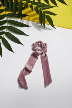 Subject shot of a pale pink velure hair scarf fixed on the scrunchie isolated on the gray and yellow surface decorated with tropic leaves.