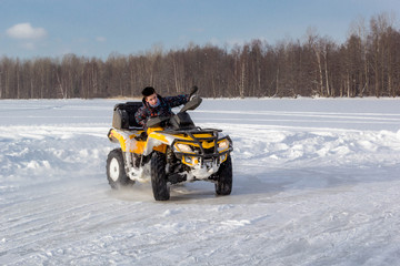 Young man rides ATV on ice on snow frozen lake in cold sunny winter day.