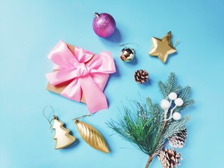 Wrapped gift box with pink bow ribbon, spruce branch, golden toys and pine cones on a blue background. Christmas and New Year flat lay photo composition. Elegant home decor