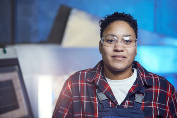 Head and shoulders portrait of mixed-race female worker smiling at camera while posing in factory...