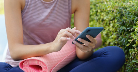 Woman use of mobile phone for online with her yoga mat at outdoor