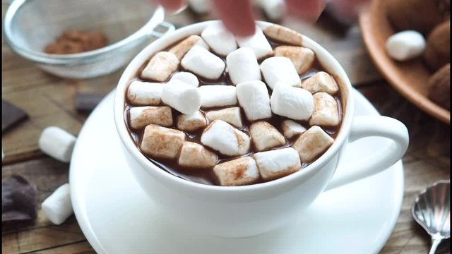 Adding marshmallow to a mug of hot chocolate. Cozy winter concept. Drink cocoa zephyr and chocolate.