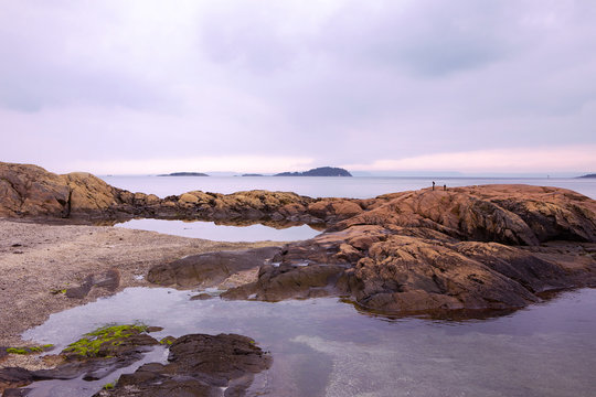 Scenic Oslo Fjord landscape, calm water, cloudy sky, rocky coast, small islands. Idyllic beach with orange rocks, tranquility. Norwegian coastline in summer. Nesodden Norway. Nesoddtangen peninsula.