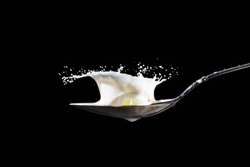 Grape drops on a spoon with milk and produces a splash of milk - isolated on black background