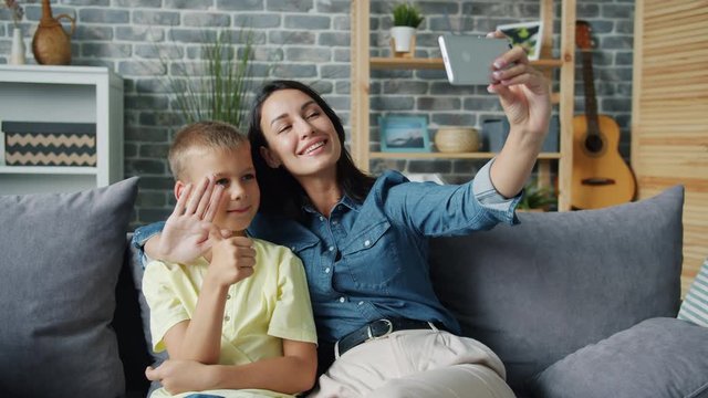 Pretty girl mother is taking selfie with cute son smiling gesturing and having fun holding smartphone with camera. Modern technology and family photographs concept.