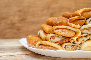 Pancakes with filling stacked pyramid on a white plate, standing on a wooden background close-up