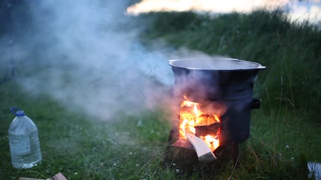 Cauldron on the river bank. Under it, a fire burns and water boils. Evening, the fishermen are going to cook fish soup.