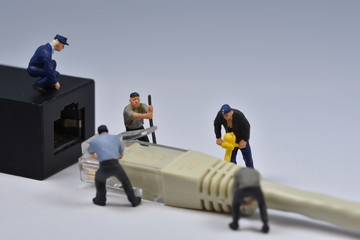 Fototapeta premium Mini workers are trying to fit a nethernet plug in a connector