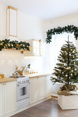 Christmas decor. Bright interior of white kitchen with decorated Christmas tree, garlands and Christmas wreaths.