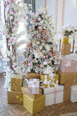 Christmas decor. The bright interior of the chic living room is decorated with an arch of decorative blue Christmas trees, gifts and white flowers. Unusual kind of Christmas tree.