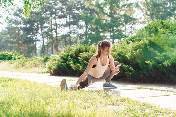 Healthy Lifestyle. Young woman in earphones outdoors listening music stretching leg watching video on smartphone joyful