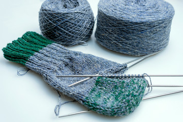 hand-knitted undersock with balls of wool on a white background