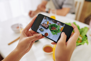 Hands of woman photographing dishes with food on smartphone to post on social media