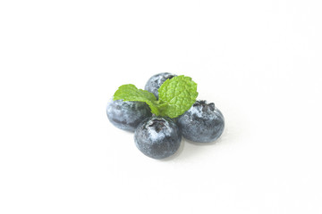 Blueberries and a mint leaf on a white background