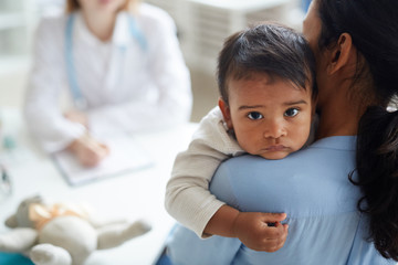 Rear view of young mother holding her little child while they visiting pediatrician at hospital