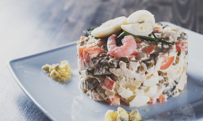Olivier salad with shrimps, eggs and vegetables in a plate on wooden table