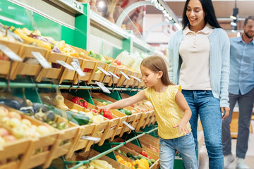Small girl with parents choosing vegetables in supermarket